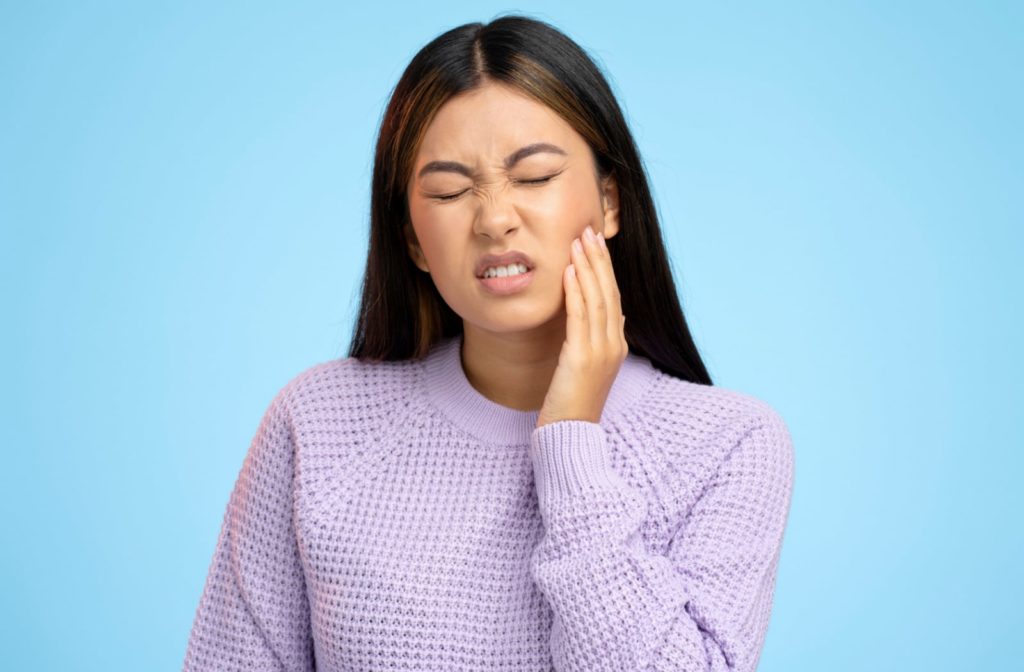 A young woman holding her left hand to the side of her jaw due to tooth pain