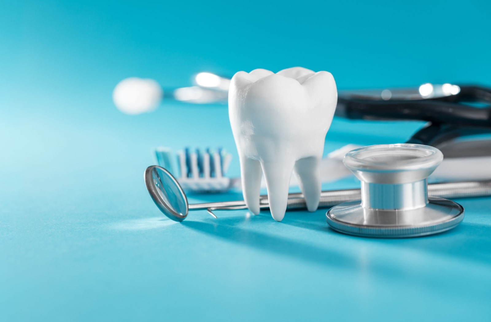 A plastic model of a tooth sitting next to a small dental mirror, a toothbrush, and a stethoscope