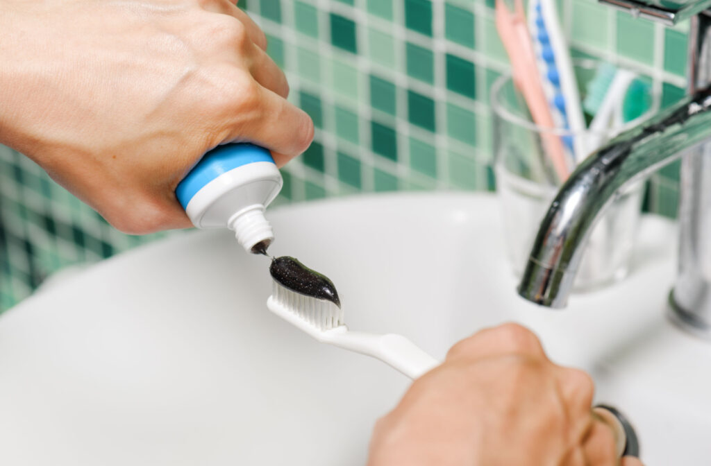 A person placing charcoal toothpaste onto their toothbrush