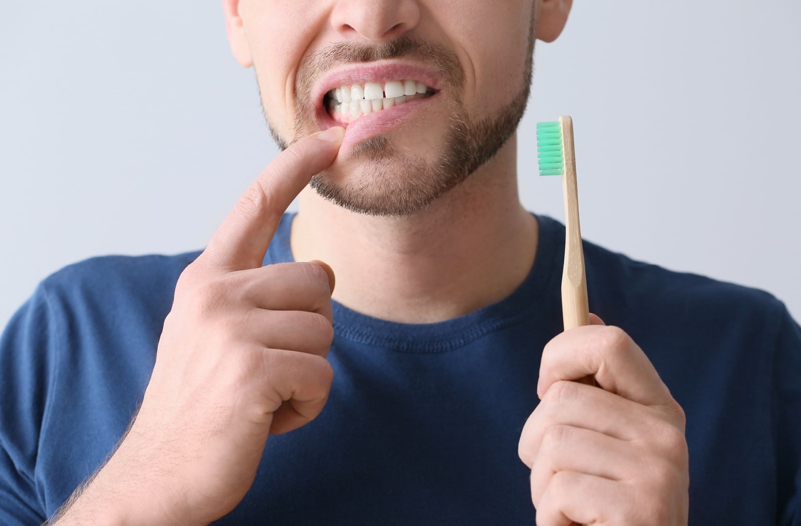 A man holding a toothbrush in his left hand and pulling down his lip slightly with his right hand to show his gumline