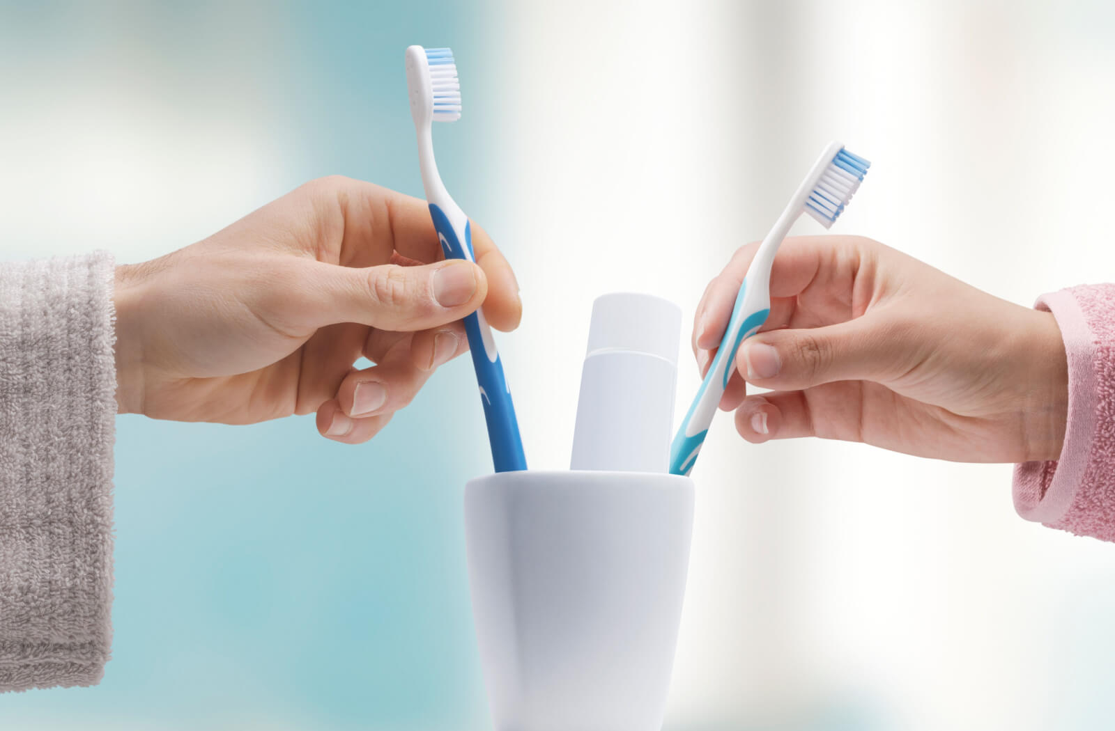 two people placing their toothbrushes into a cup