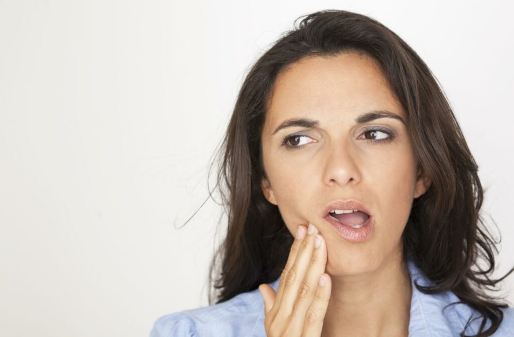 A close-up image of a woman holding her face in discomfort due to a cavity.