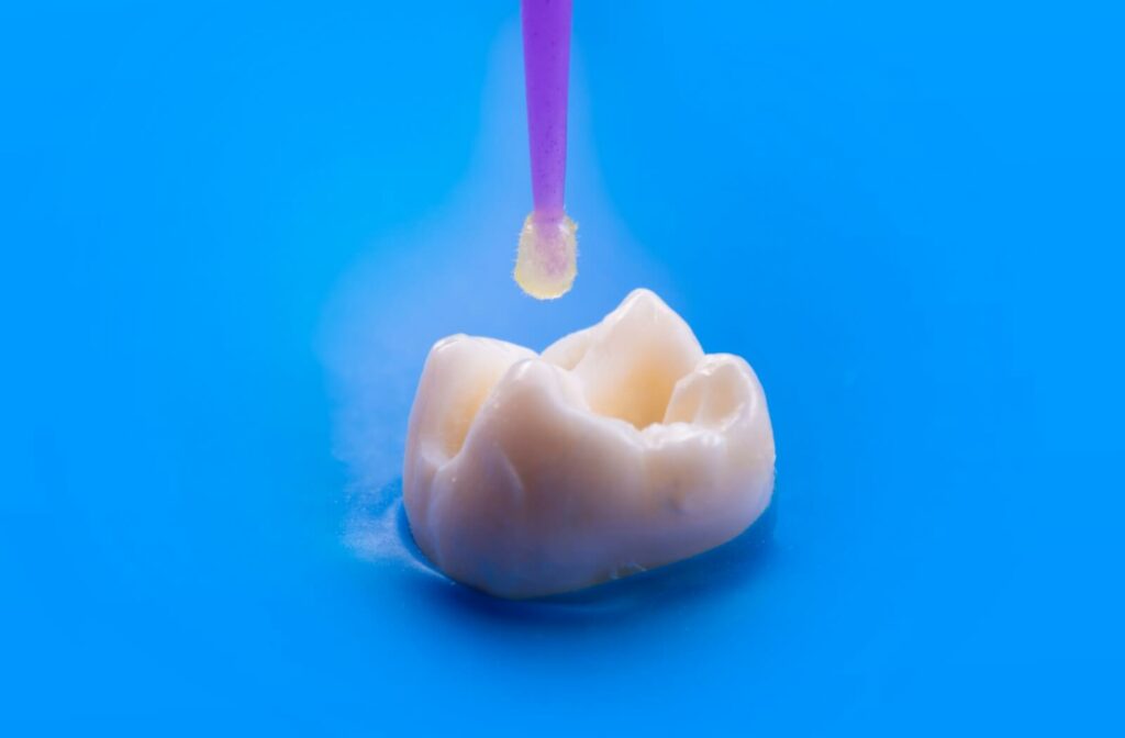 A close-up of a microbrush dipped in resin, being held over a damaged tooth. The brush is positioned to paint the resin on to the damaged tooth area.