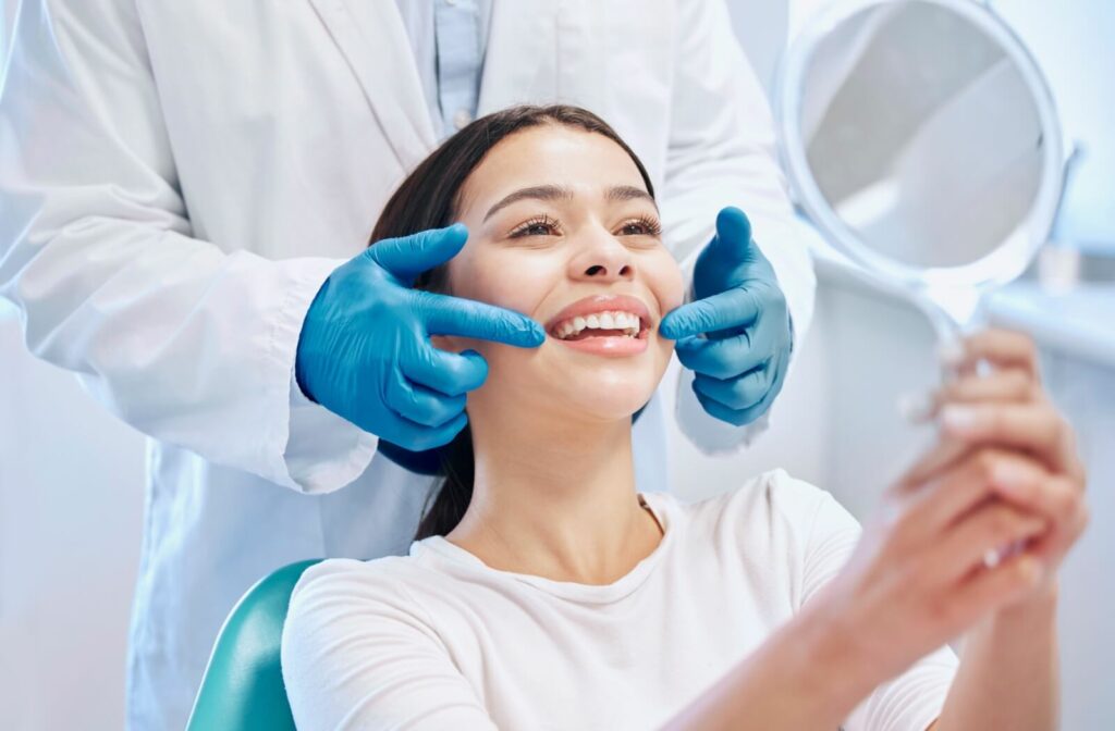 A woman smiling at a mirror while a dentist shows her the results of her teeth whitening procedure.