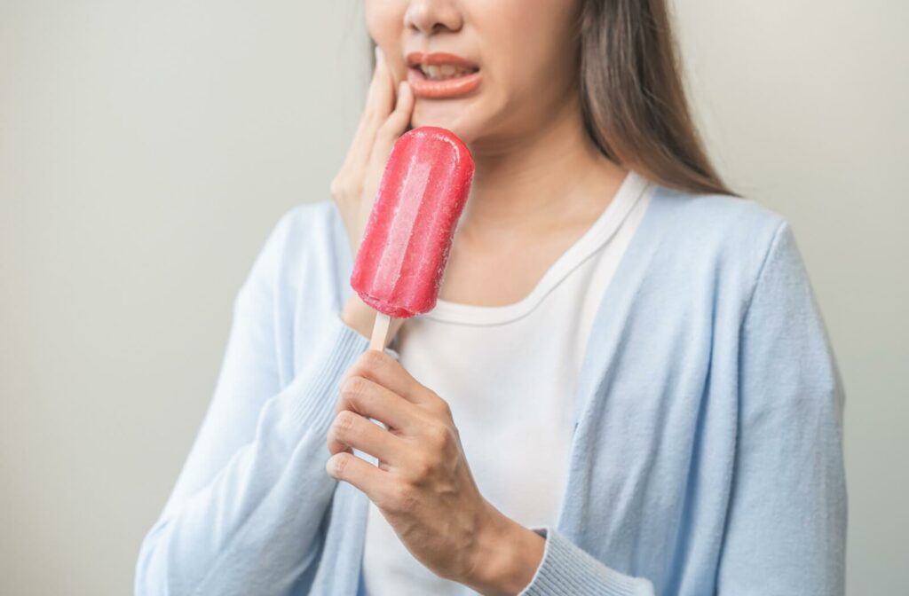 A young woman wincing in pain trying to eat a popsicle after a tooth extraction.