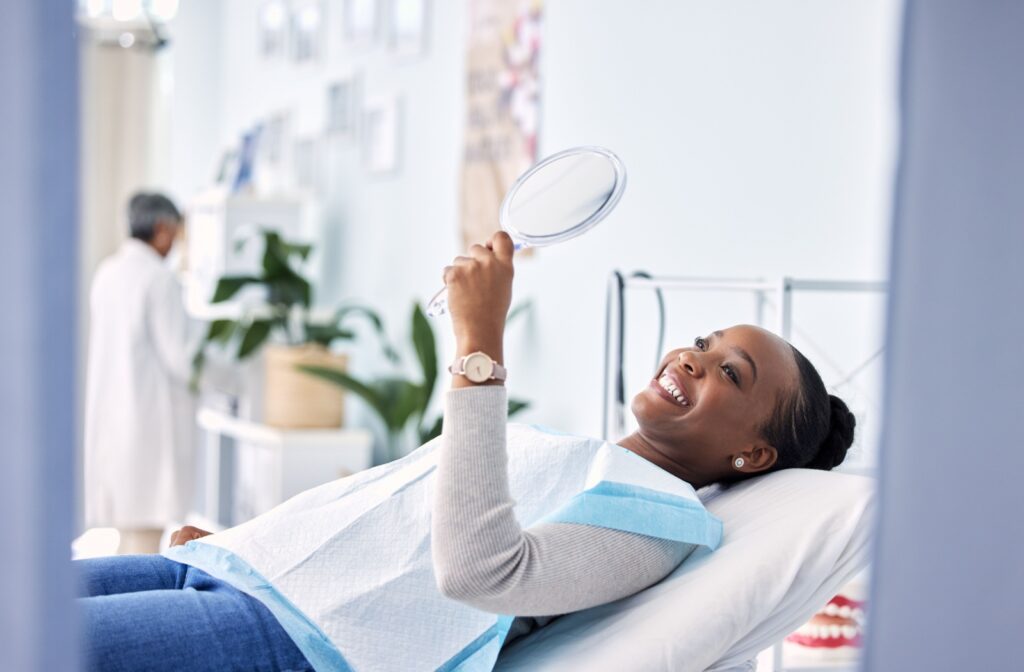 An adult admires their freshly cleaned teeth in a mirror after the dental hygienist finished the professional dental cleaning.