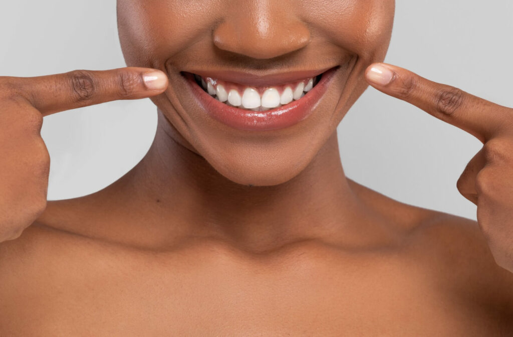 A person smiles happily while pointing with both hands towards their bright white teeth