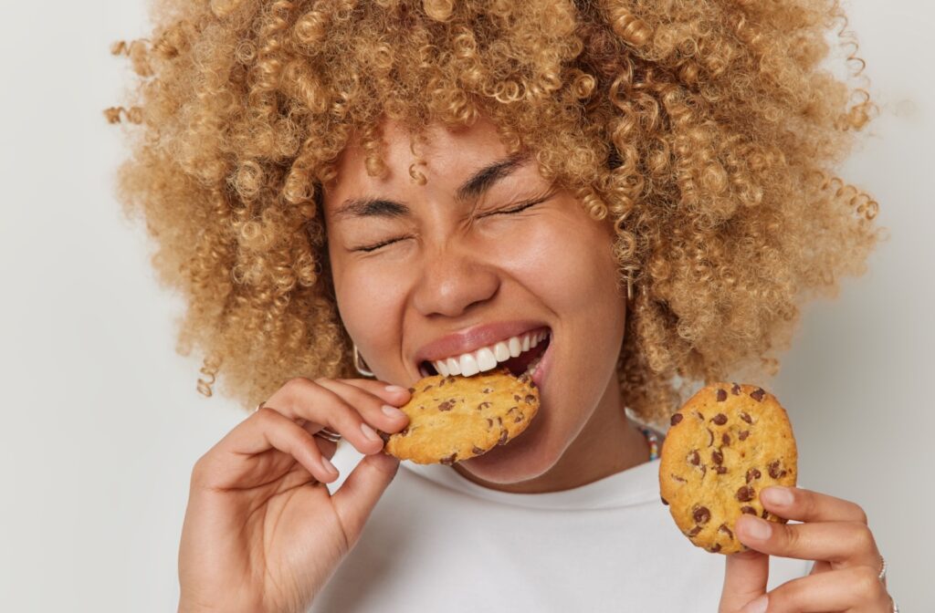 A young adult biting into a cookie and wincing in pain as she deals with a chipped tooth.