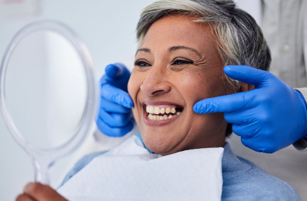 A patient smiling into a mirror after a dental appointment where her dentist fixed her chipped tooth.