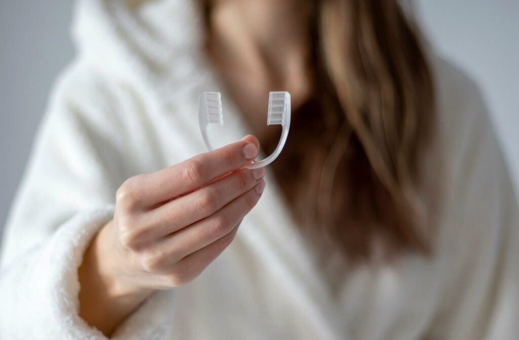 A focused close-up image of a person in a white bathrobe holding up a clear mouthguard before going to bed.