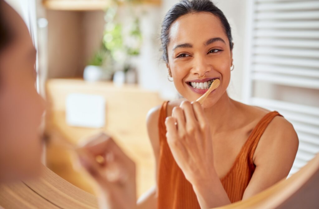 A person looking in the mirror while brushing their teeth with fluoride toothpaste.