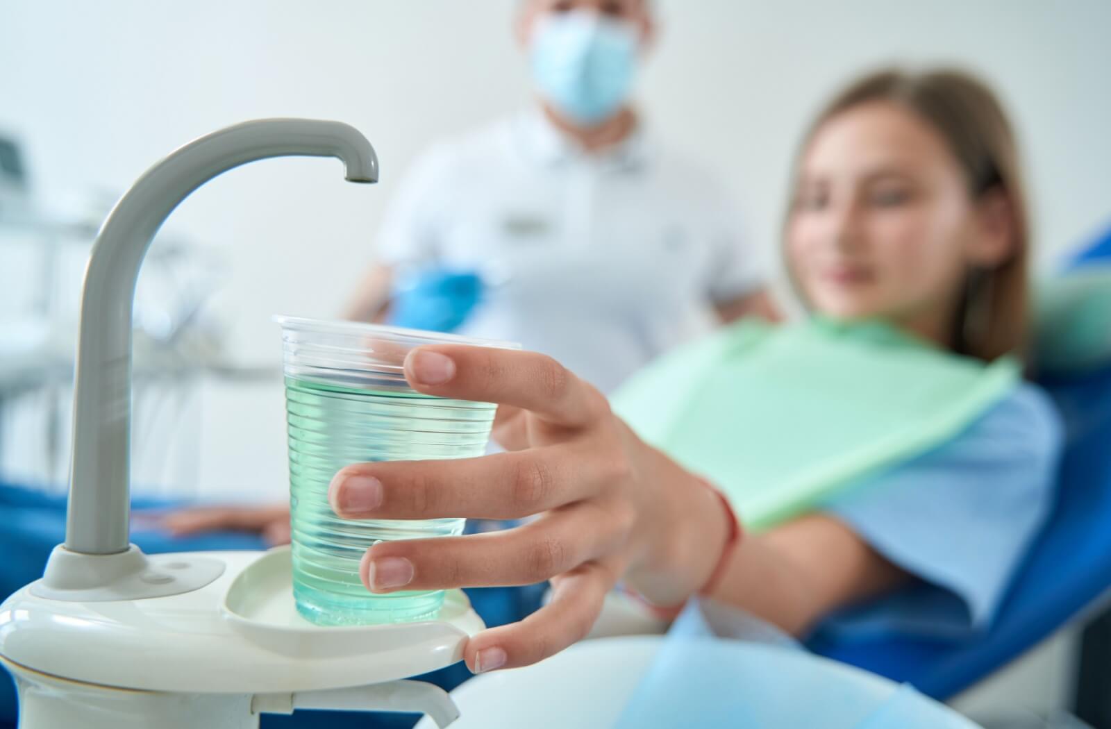 Dentist patient holding a plastic cup of green mouthwash while seated in a dental chair