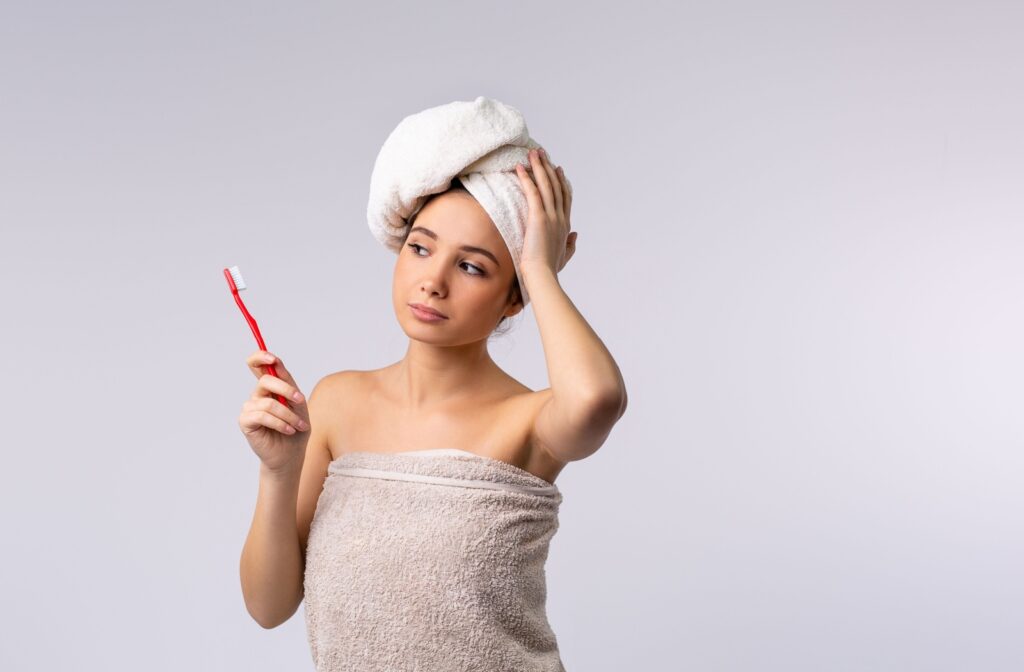 A person looking at a toothbrush wondering about teeth while wearing a towel on their head after a shower.