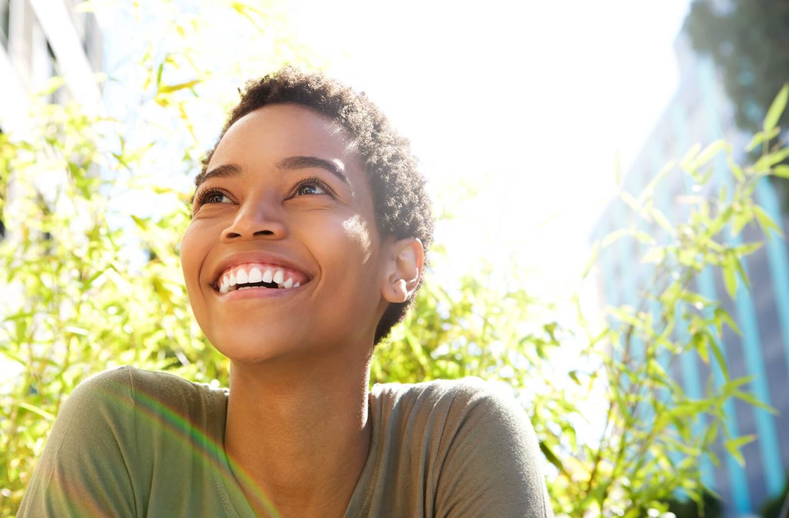 A person smiles in the sunlight outdoors, revealing their white teeth.