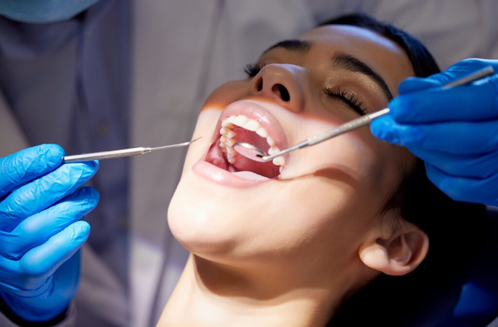 A close-up of a person receiving a dental cleaning from a gloved dental professional using dental tools.