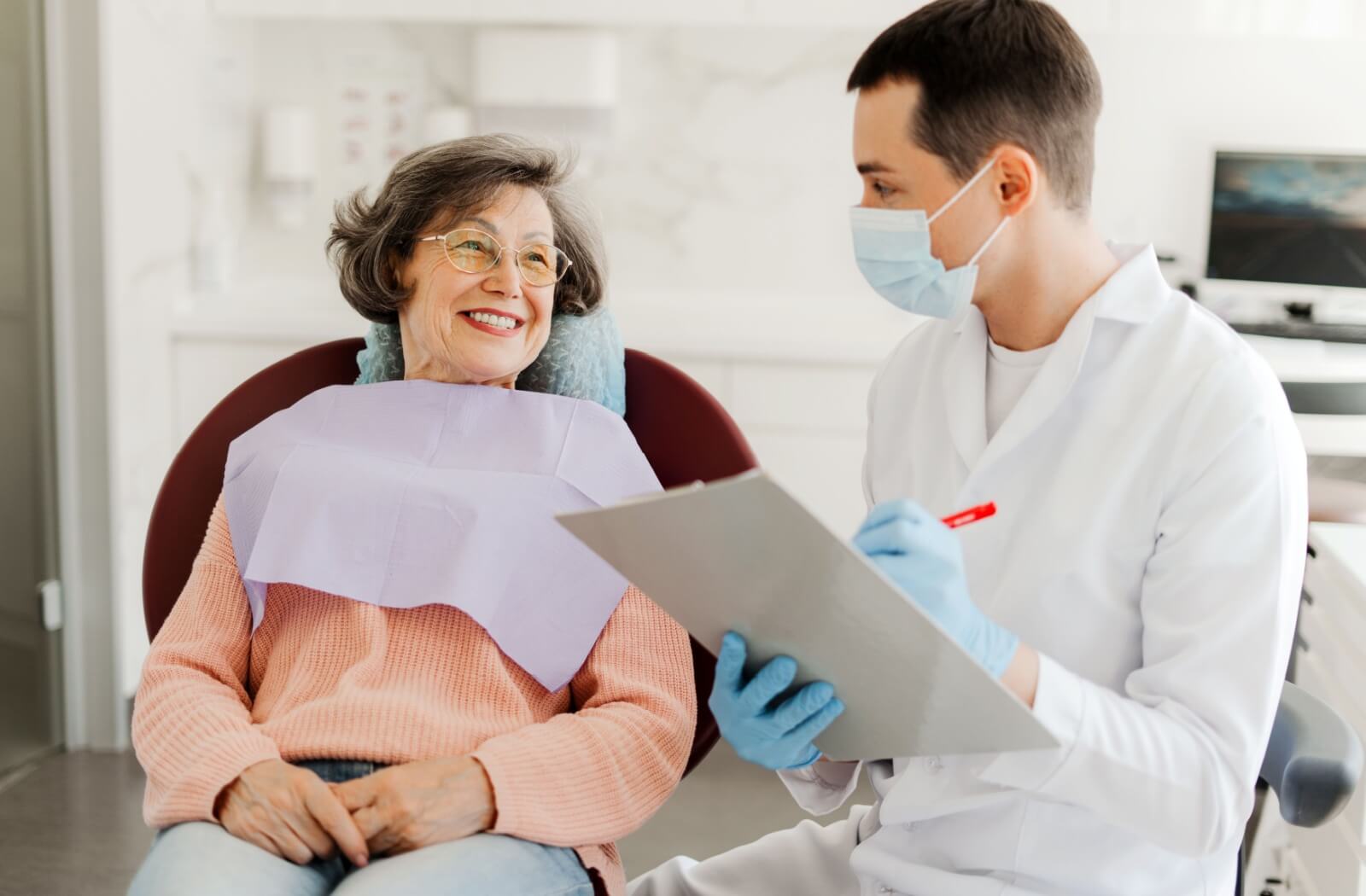A person sitting in a dental chair smiling at the dentist who is holding a clipboard.